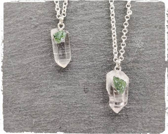 May include: Two silver necklaces with clear quartz crystal pendants. Each pendant has a small green stone embedded in it.