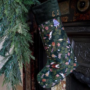 May include: A dark green velvet Christmas stocking featuring a festive pattern of Nutcracker-themed figures, sweets, and ornaments. The cuff is made of solid dark green velvet and is embroidered with the gold-coloured initials E.S. in a script font.