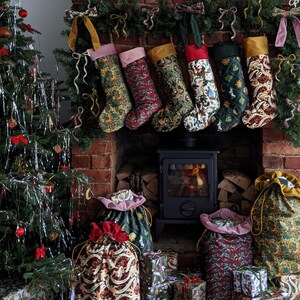 May include: A Christmas display with a decorated tree, stockings, and gifts. Six patterned stockings hang above a fireplace with a lit fire. Gift bags and wrapped presents are arranged in front of the fireplace, creating a festive holiday scene.