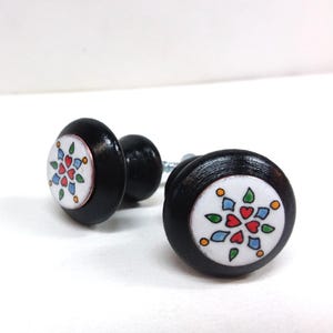 Peut inclure: Deux boutons en bois noir avec des incrustations en céramique blanche. Les incrustations présentent un motif floral coloré avec des accents rouges, bleus, verts et jaunes.