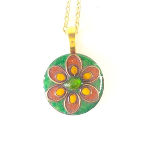 May include: A gold chain necklace with a round pendant featuring a green, orange and yellow enamel flower design.