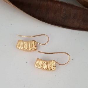 May include: A pair of gold-toned earrings with a textured, curved design. The earrings have a simple hook closure.