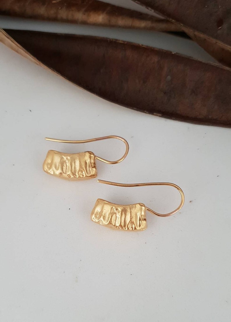 May include: A pair of gold-toned earrings with a textured, curved design. The earrings have a simple hook closure.