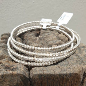 May include: A set of five silver beaded bracelets. The bracelets are stacked on top of each other and are made of small, round beads.