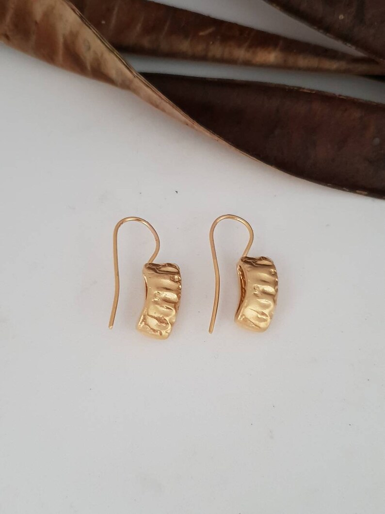 May include: A pair of gold hoop earrings with a textured surface. The earrings have a simple hook closure.