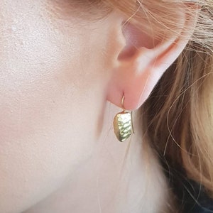 May include: Gold dangle earrings with a textured, hammered design. The earrings are a simple, minimalist style.