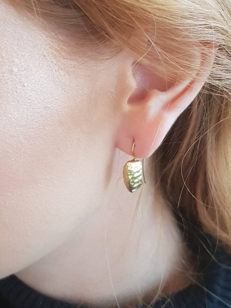 May include: Gold dangle earrings with a textured, hammered design. The earrings are a simple, minimalist style.