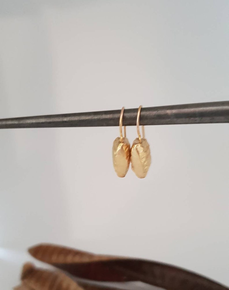 May include: A pair of gold-toned earrings with a textured, hammered finish. The earrings are oval-shaped and hang from a simple wire hook.