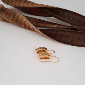 May include: A pair of gold-toned earrings with a textured, geometric design. The earrings have a simple hook closure.