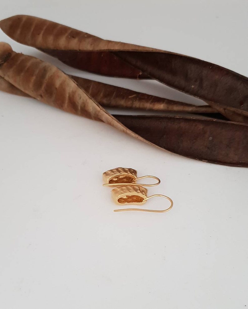 May include: A pair of gold-toned earrings with a textured, geometric design. The earrings have a simple hook closure.