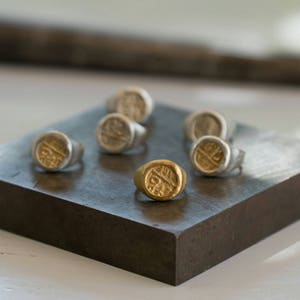 May include: A collection of seven silver and gold rings with a circular design on a dark gray surface. The rings are arranged in a semi-circle.