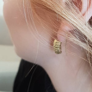 May include: A close-up of a person's ear with a gold hoop earring. The earring is simple and has a smooth finish.