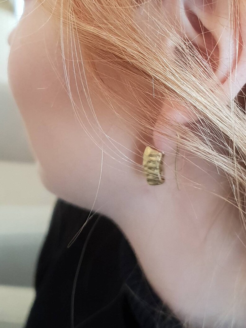 May include: A close-up of a person's ear with a gold hoop earring. The earring is simple and has a smooth finish.