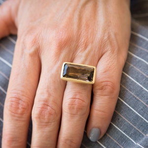 Könnte beinhalten: Ein goldener Ring mit einem rechteckigen, rauchquarzfarbenen Edelstein.