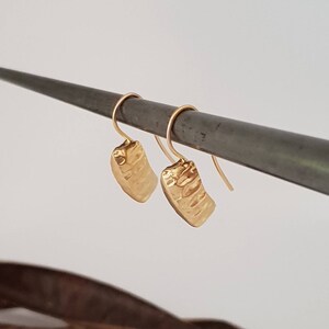 May include: A pair of gold hammered rectangle dangle earrings. The earrings are hanging from a metal rod.