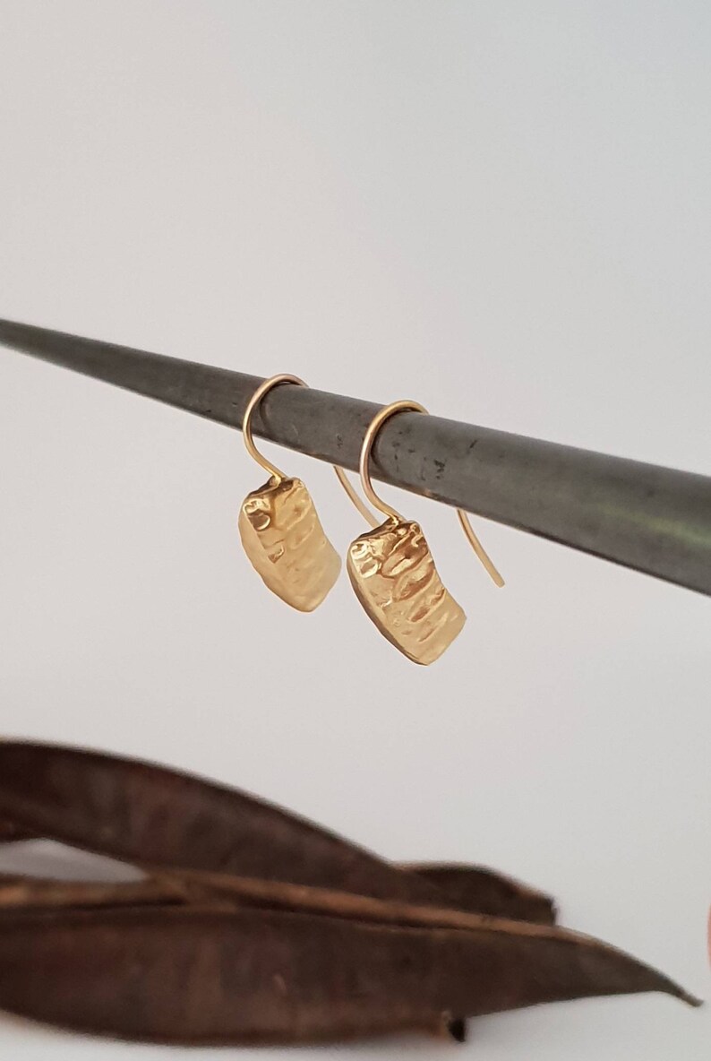 May include: A pair of gold hammered rectangle dangle earrings. The earrings are hanging from a metal rod.