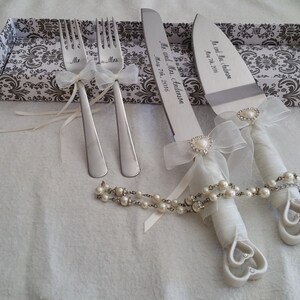 May include: A white cake knife and two forks with pearl and ribbon embellishments. The knife is engraved with "Mr. and Mrs. Anderson" and the date "June 2016".