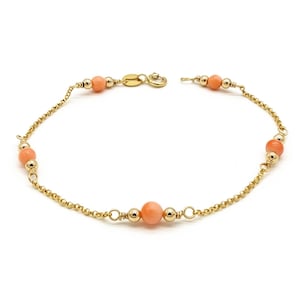 Peut inclure: Un bracelet en or délicat orné de perles de corail. Le bracelet présente une fine chaîne avec de petites perles d'or parsemées le long de la chaîne. Les perles de corail sont d'une couleur rose pêche douce. Le bracelet est sécurisé par un fermoir en or.