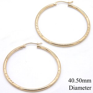 May include: A pair of gold hoop earrings with a textured surface. The earrings are 40.50mm in diameter.