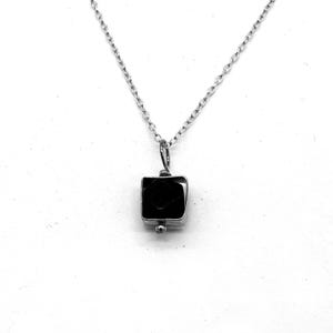 May include: A silver necklace with a square, black pendant. The pendant is set in silver and suspended from a delicate chain. A small, round silver bead is at the base of the pendant.
