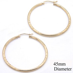 May include: A pair of gold hoop earrings with a textured surface. The earrings are 45mm in diameter.