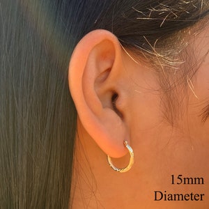 May include: Gold hoop earrings with a twisted design. The earrings are 15mm in diameter.