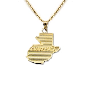 Può includere: Una collana con pendente dorato raffigurante il contorno dettagliato del Guatemala. Il pendente reca la scritta "GUATEMALA". La collana ha una catena delicata e una semplice chiusura.