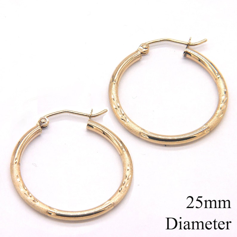 May include: A pair of gold hoop earrings with a textured design. The earrings are 25mm in diameter.