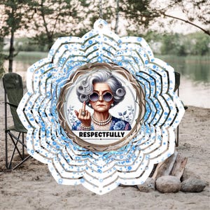 May include: A decorative wind spinner featuring a portrait of an elderly woman wearing sunglasses and a pearl necklace, giving the middle finger. The image is surrounded by a white and blue floral design, with the word "RESPECTFULLY" below the portrait.
