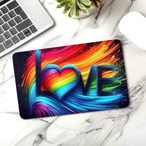 May include: A rectangular mousepad with a vibrant, colorful design. The word "LOVE" is prominently displayed, with the "O" replaced by a rainbow-colored heart. The background features streaks of red, orange, yellow, green, and blue.
