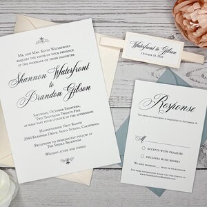 May include: A white wedding invitation with black calligraphy text. The invitation reads "Shannon Waterfront to Brandon Gibson" and includes the date, time, and location of the wedding. A separate white card with a blue envelope reads "Response" and includes options for guests to RSVP.