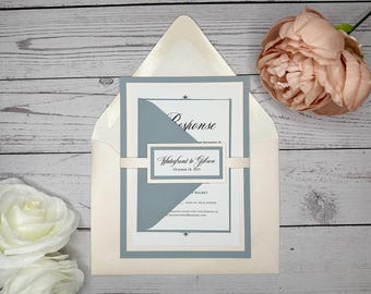 May include: A wedding invitation with a light blue and white color scheme. The invitation is folded in half and has a white envelope. The text on the invitation reads "Waterfront to Gibson, October 18, 2023".