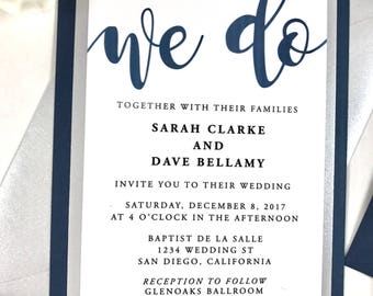 May include: A wedding invitation with a navy blue and silver border. The invitation reads "We do" in a cursive font. The text below reads "Together with their families, Sarah Clarke and Dave Bellamy invite you to their wedding, Saturday, December 8, 2017 at 4 o'clock in the afternoon, Baptist de la Salle, 1234 Wedding St, San Diego, California. Reception to follow, Glenoaks Ballroom, 5678 Wedding Blvd, San Diego, California."
