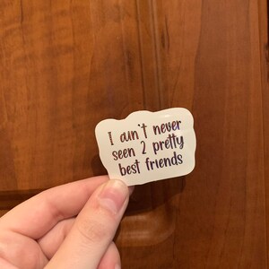May include: White sticker with a pink and red glittery design. The sticker says "I ain't never seen 2 pretty best friends".