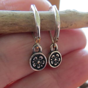 May include: A pair of silver hoop earrings with a small black flower charm hanging from each hoop. The earrings are marked "925" on the back.