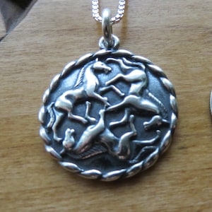 May include: Silver pendant necklace featuring a circular design with four horses in a circular pattern. The horses are in a stylized, almost abstract design.