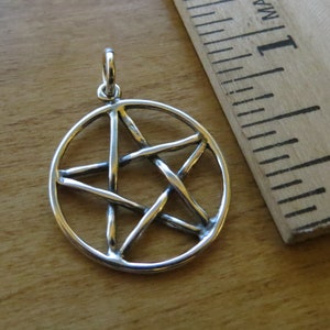 May include: Silver pendant featuring a pentacle, a five-pointed star within a circle. The star is made of thick, twisted wire.