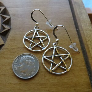 May include: A pair of silver earrings featuring a pentacle design. The earrings are approximately the size of a 10 pence coin.
