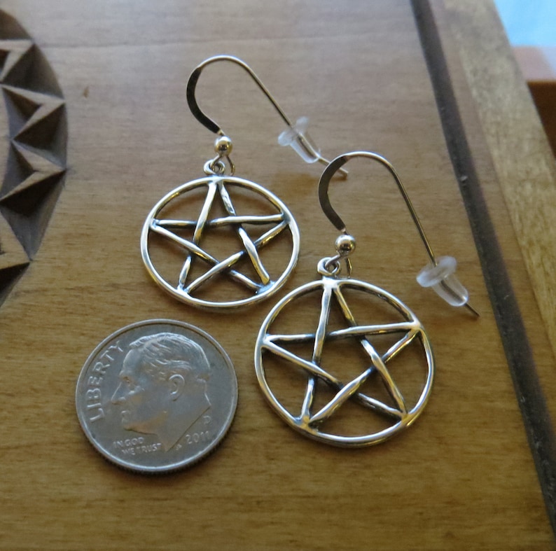 May include: A pair of silver earrings featuring a pentacle design. The earrings are approximately the size of a 10 pence coin.
