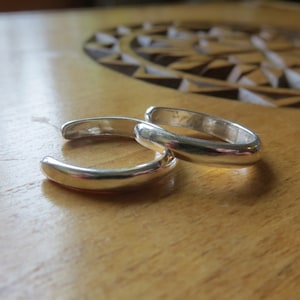 May include: Two silver ear cuffs, one on top of the other, on a wooden surface.