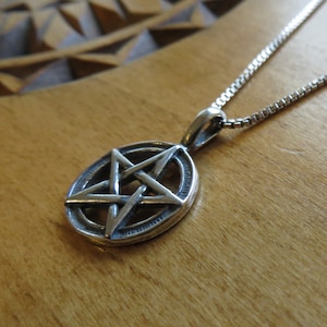 May include: A silver pendant necklace with a pentagram design. The pendant is round and has a detailed five-pointed star inside.