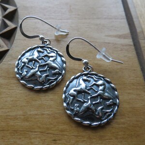 May include: Silver dangle earrings with a circular design featuring five horses in a Celtic knot pattern.
