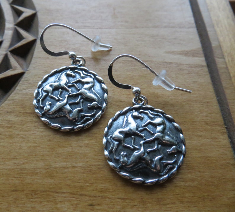 May include: Silver dangle earrings with a circular design featuring five horses in a Celtic knot pattern.