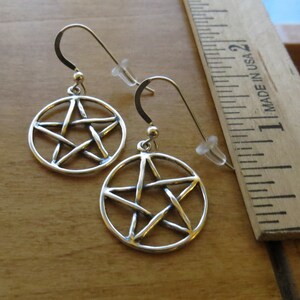 May include: A pair of silver earrings featuring a pentacle design. The earrings are approximately 2.5 cm in diameter.