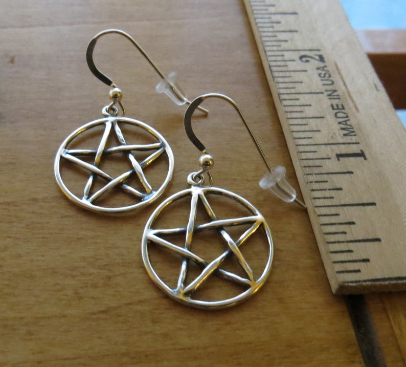 May include: A pair of silver earrings featuring a pentacle design. The earrings are approximately 2.5 cm in diameter.