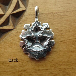Op de afbeelding: Zilveren hanger met een gedetailleerd ontwerp van een gezicht met een kroon van bladeren. De achterkant van de hanger is gestempeld met "925", wat aangeeft dat het van sterling zilver is gemaakt.