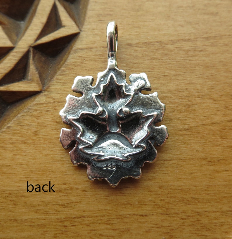 Op de afbeelding: Zilveren hanger met een gedetailleerd ontwerp van een gezicht met een kroon van bladeren. De achterkant van de hanger is gestempeld met "925", wat aangeeft dat het van sterling zilver is gemaakt.