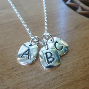 Puede incluir: Un collar de plata con tres colgantes de plata, cada uno con una letra. Las letras son A, B y C.