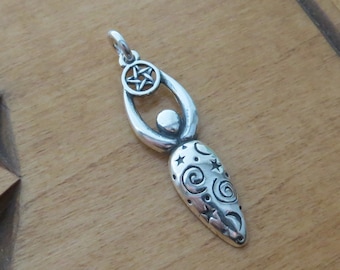 May include: A silver pendant in the shape of a stylized female figure. The pendant features a pentagram at the top, a central sphere, and a decorated lower section with stars and swirls. The pendant is designed with a loop for a chain.