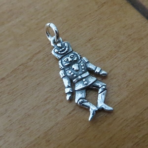 May include: Silver charm of a nutcracker in a standing pose with a whimsical expression. The charm has a loop at the top for attaching to a bracelet or necklace.